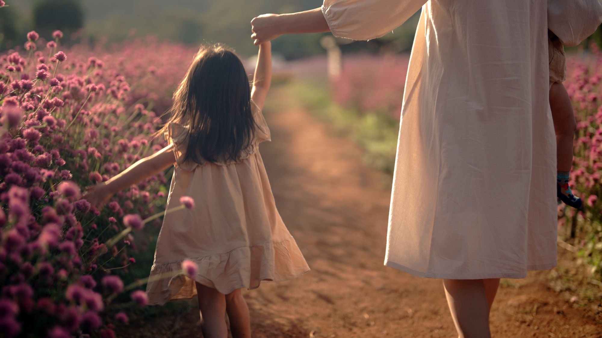 A mother and daughter walking hand in hand along a flower path