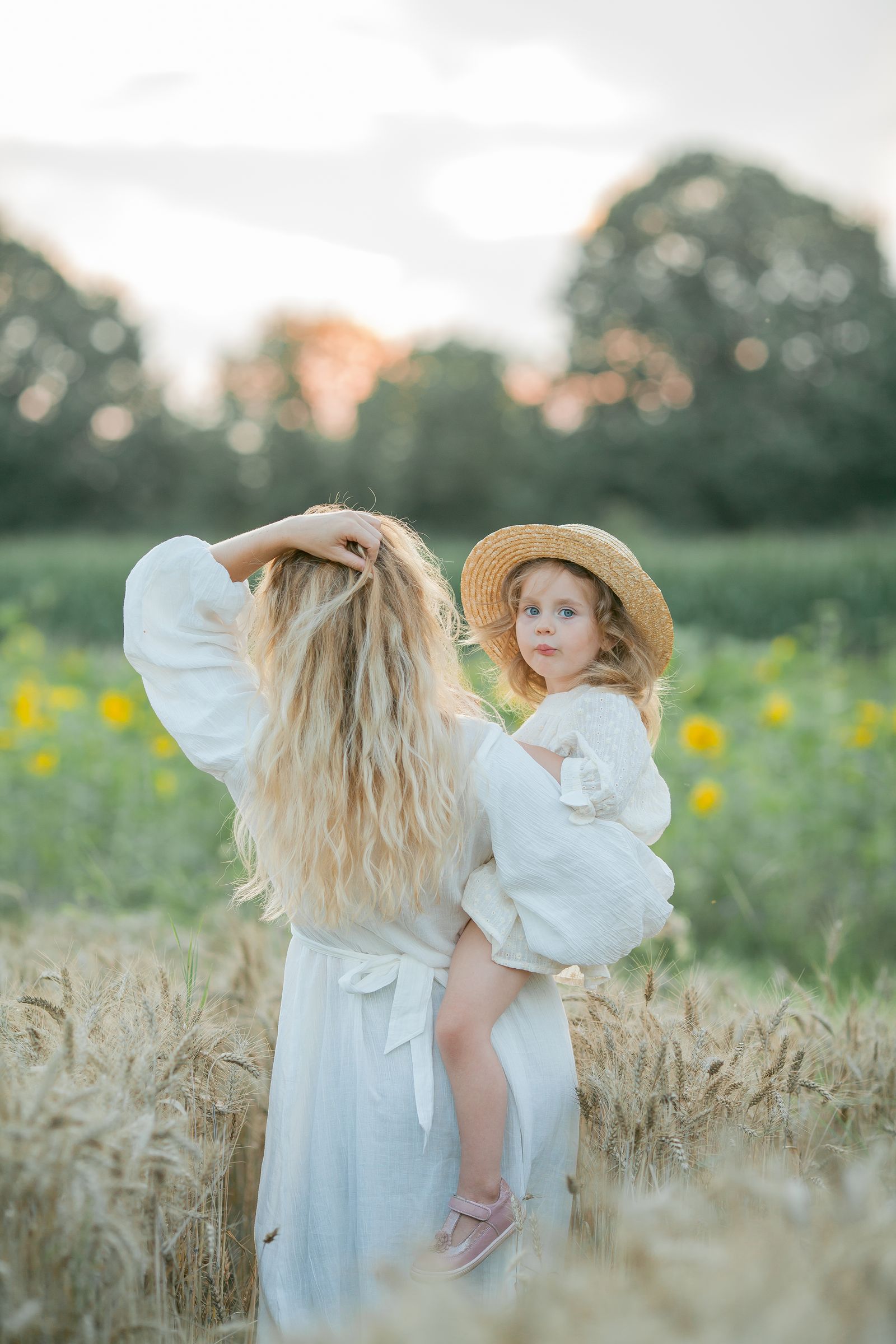 A mother carrying her daughter through a wheat field at dusk
