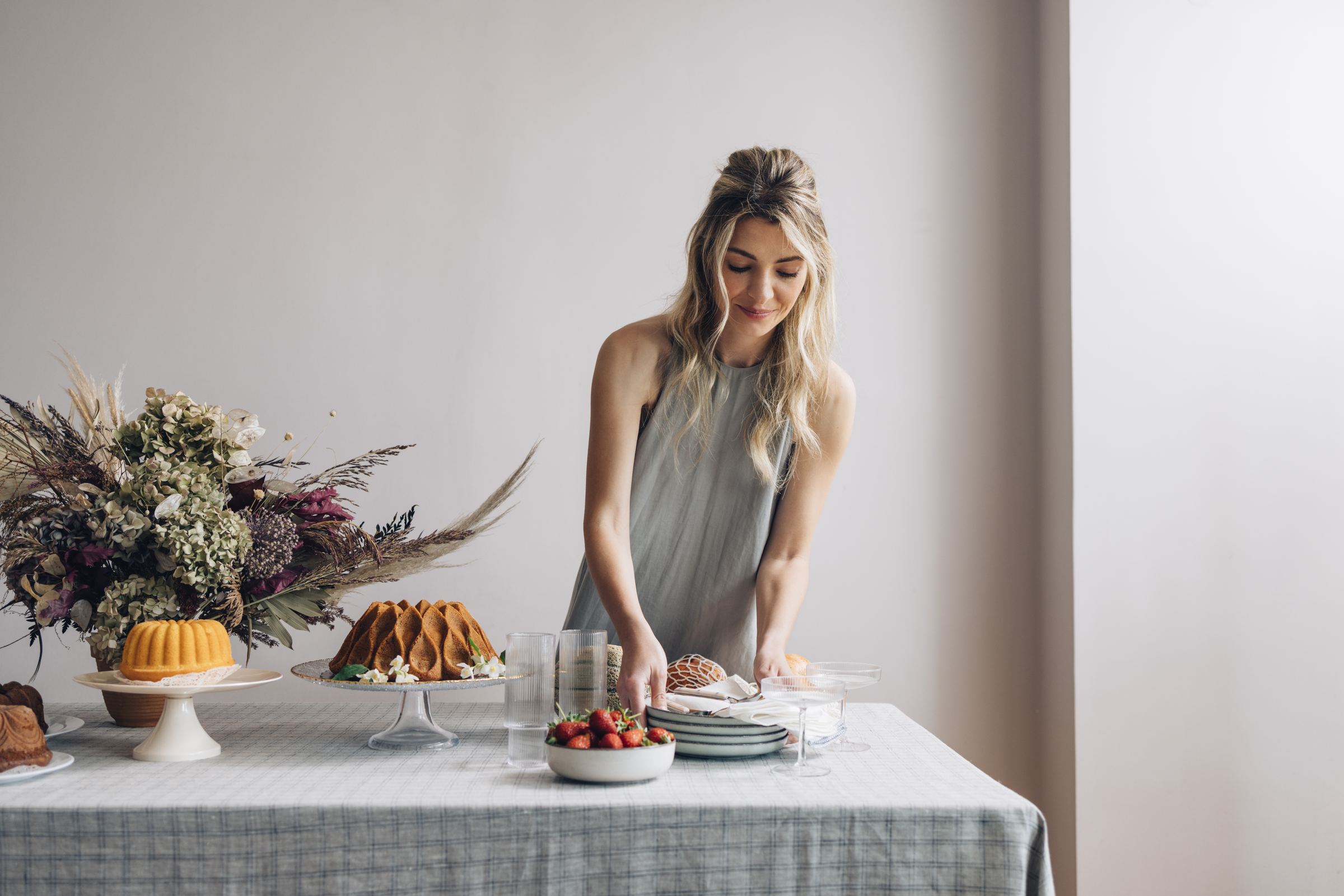 A woman laying a celebration table with cakes, strawberries and flowers